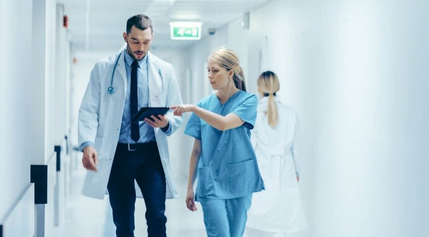 Female Surgeon and Doctor Walk Through Hospital Hallway checking documents