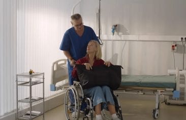 Healthcare Customer Service: Male orderly pushing senior female patient being discharged from hospital in wheelchair. Senior man nurse pushing wheelchair with aged woman leaving hospital after recovery
