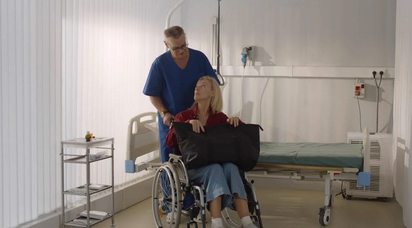 Healthcare Customer Service: Male orderly pushing senior female patient being discharged from hospital in wheelchair. Senior man nurse pushing wheelchair with aged woman leaving hospital after recovery